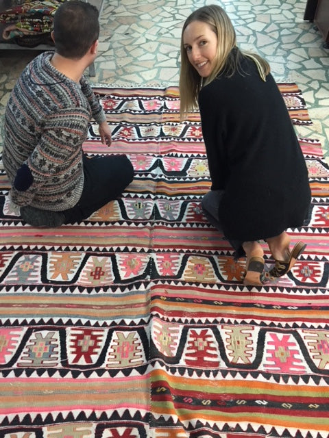 Artemis founder Milicent Armstrong kneeling on a colorful kilim carpet, with a friend facing away from the camera.