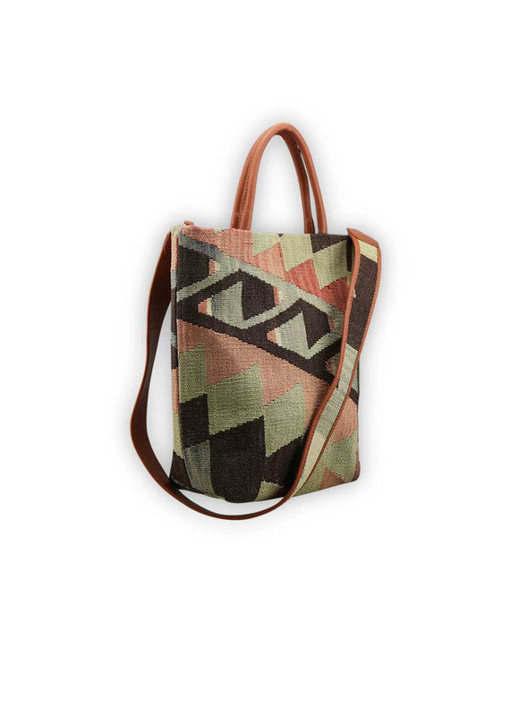 The Artemis Design Co. Sumak Kilim Tote boasts a captivating fusion of tradition and modernity. Crafted with a chic black base, this tote features a vibrant Sumak Kilim pattern adorned with bold accents of red, alongside hues of black, blue, green, and white. The dynamic color palette infuses a contemporary edge into the timeless design, making it a standout accessory for any occasion. (Side View)