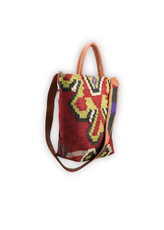 The Artemis Design Co. Sumak Kilim Tote is a striking blend of traditional craftsmanship and contemporary style. Made with premium brown leather accents, this tote features a vibrant Sumak Kilim pattern in a rich array of colors, including apple green, black, red, white, and blue. The harmonious combination of these hues creates a bold and dynamic look, perfect for adding a pop of personality to any ensemble. (Side View)