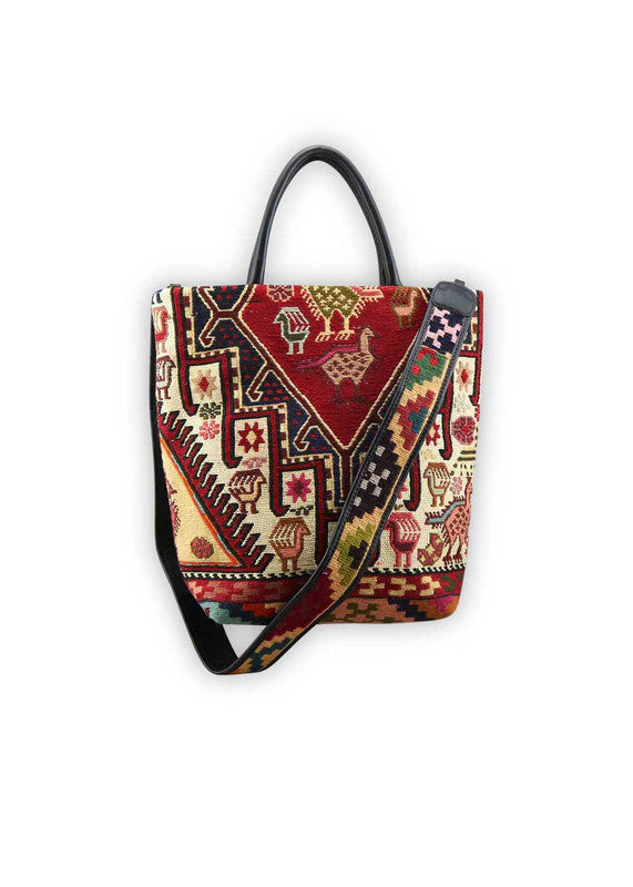 The Artemis Design Co. Sumak Kilim Tote is a stylish and versatile accessory crafted with a blend of sumptuous brown leather and vibrant, eye-catching colors. The tote features a traditional Sumak Kilim pattern in a spectrum of hues including red, white, blue, green, peach, orange, and yellow. This eclectic color combination lends a dynamic and playful aesthetic to the bag, making it a statement piece for any outfit or occasion. (Front View)