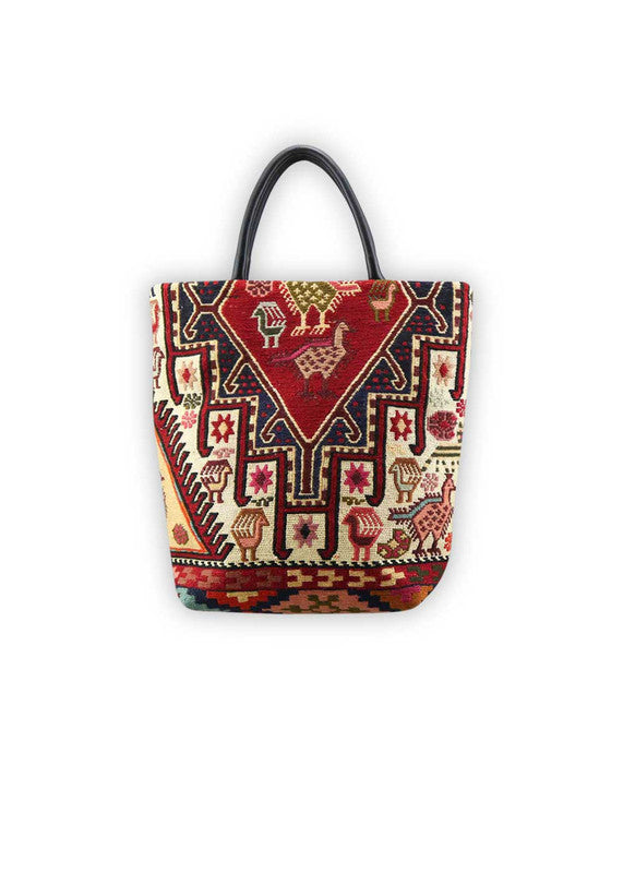 The Artemis Design Co. Sumak Kilim Tote is a stylish and versatile accessory crafted with a blend of sumptuous brown leather and vibrant, eye-catching colors. The tote features a traditional Sumak Kilim pattern in a spectrum of hues including red, white, blue, green, peach, orange, and yellow. This eclectic color combination lends a dynamic and playful aesthetic to the bag, making it a statement piece for any outfit or occasion. (Front View)