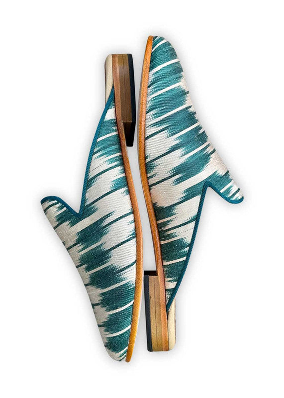 The Summer Silk Ikats slippers in a stunning color combination of teal and white are a fashionable and comfortable choice for the summer season. Made from lightweight silk ikat fabric, these slippers showcase a blend of colors that evoke a sense of freshness and serenity. The vibrant teal hue adds a pop of color, while the crisp white complements and balances the overall design. (Side View)