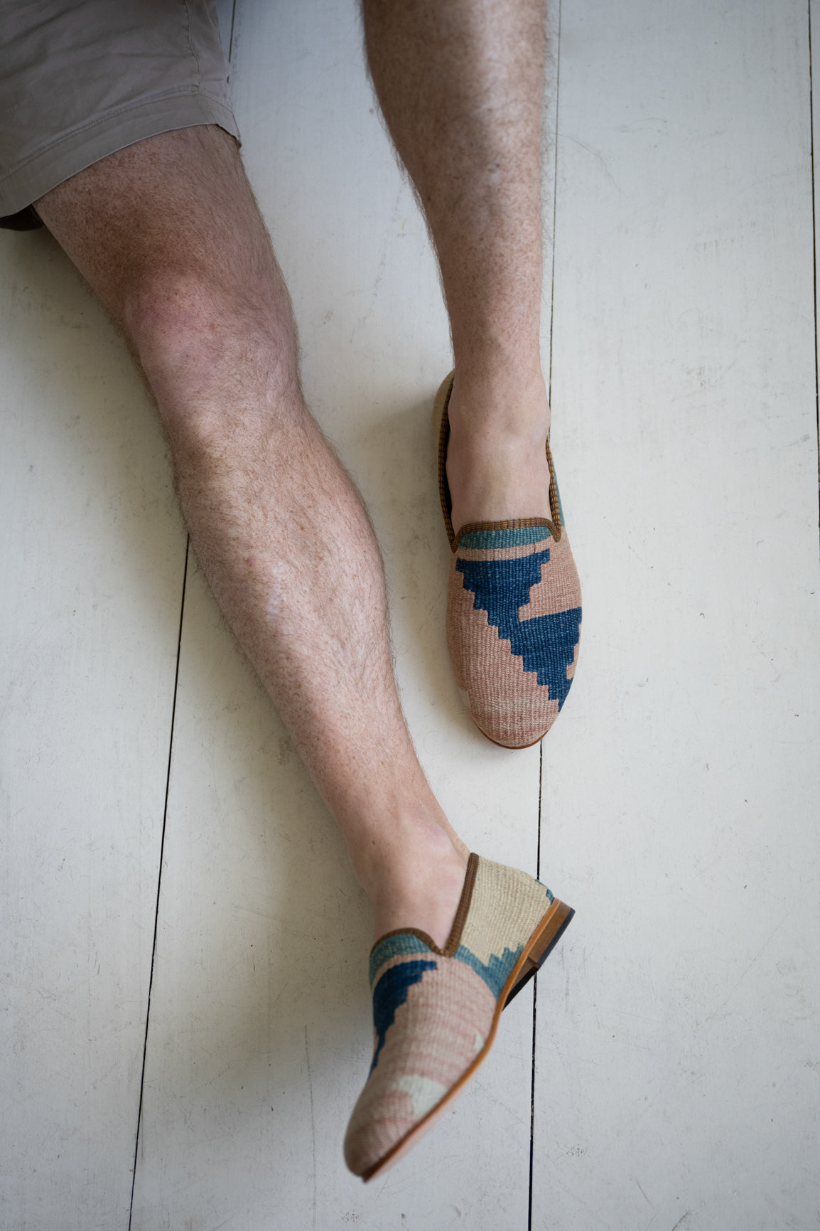 Man sitting on a floor wearing light pink and blue men's kilim loafers