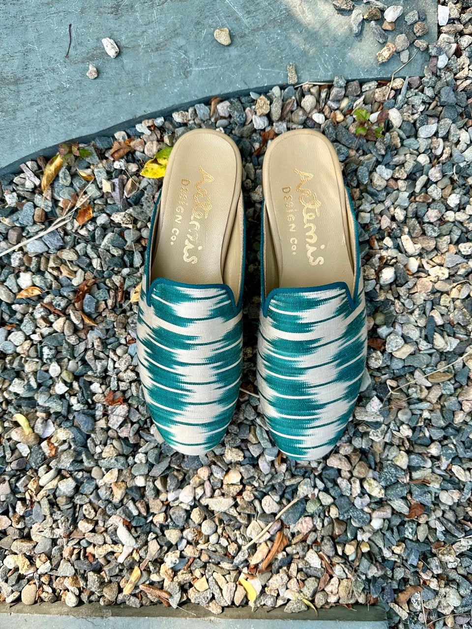 The Summer Silk Ikats slippers in a stunning color combination of teal and white are a fashionable and comfortable choice for the summer season. Made from lightweight silk ikat fabric, these slippers showcase a blend of colors that evoke a sense of freshness and serenity. The vibrant teal hue adds a pop of color, while the crisp white complements and balances the overall design. (Front View)