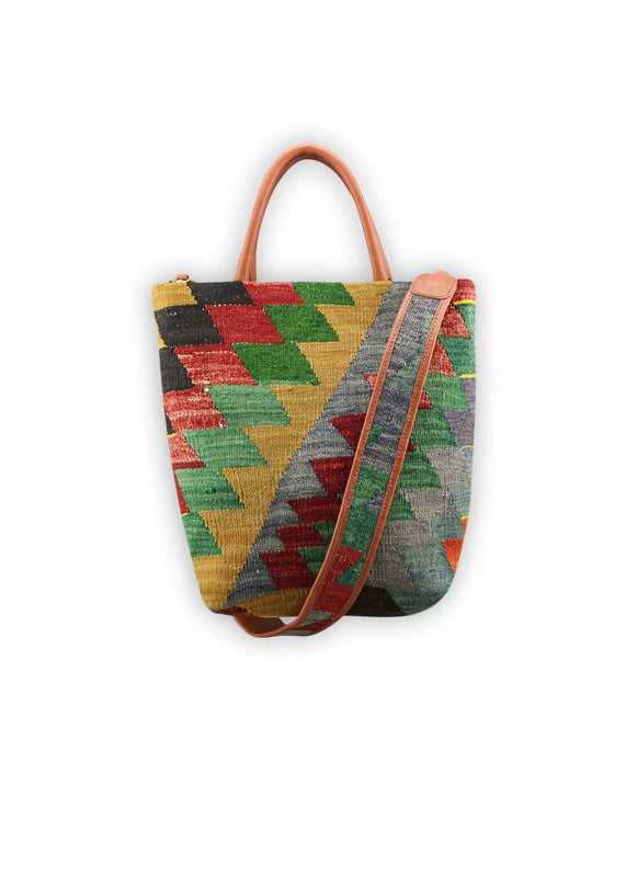 The Artemis Design Co. Sumak Kilim Tote combines timeless elegance with vibrant flair. Crafted with luxurious brown leather accents, this tote showcases a captivating Sumak Kilim pattern featuring hues of mustard, black, red, green, and blue. The sophisticated color palette creates a striking contrast against the rich leather, making this tote a standout accessory for any occasion. (Front View)